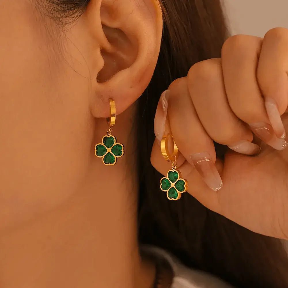 Gold hoop earrings with green clover charms worn by a person.